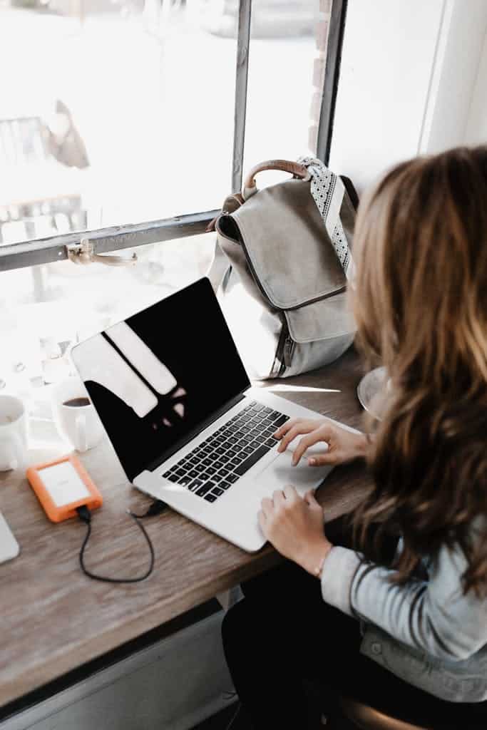 A young woman works remotely at a café, using her laptop and external hard drive to read Fabienne Louis latest energy healing blog on personal growth and transformation tools in health, money, career, relationships.